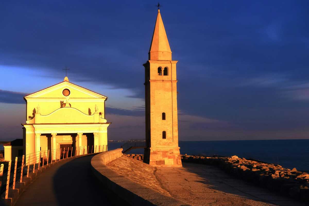 Primo piano delle sculture della Scogliera Viva con il mare sullo sfondo, passanti che osservano le opere, atmosfera artistica e rilassata.